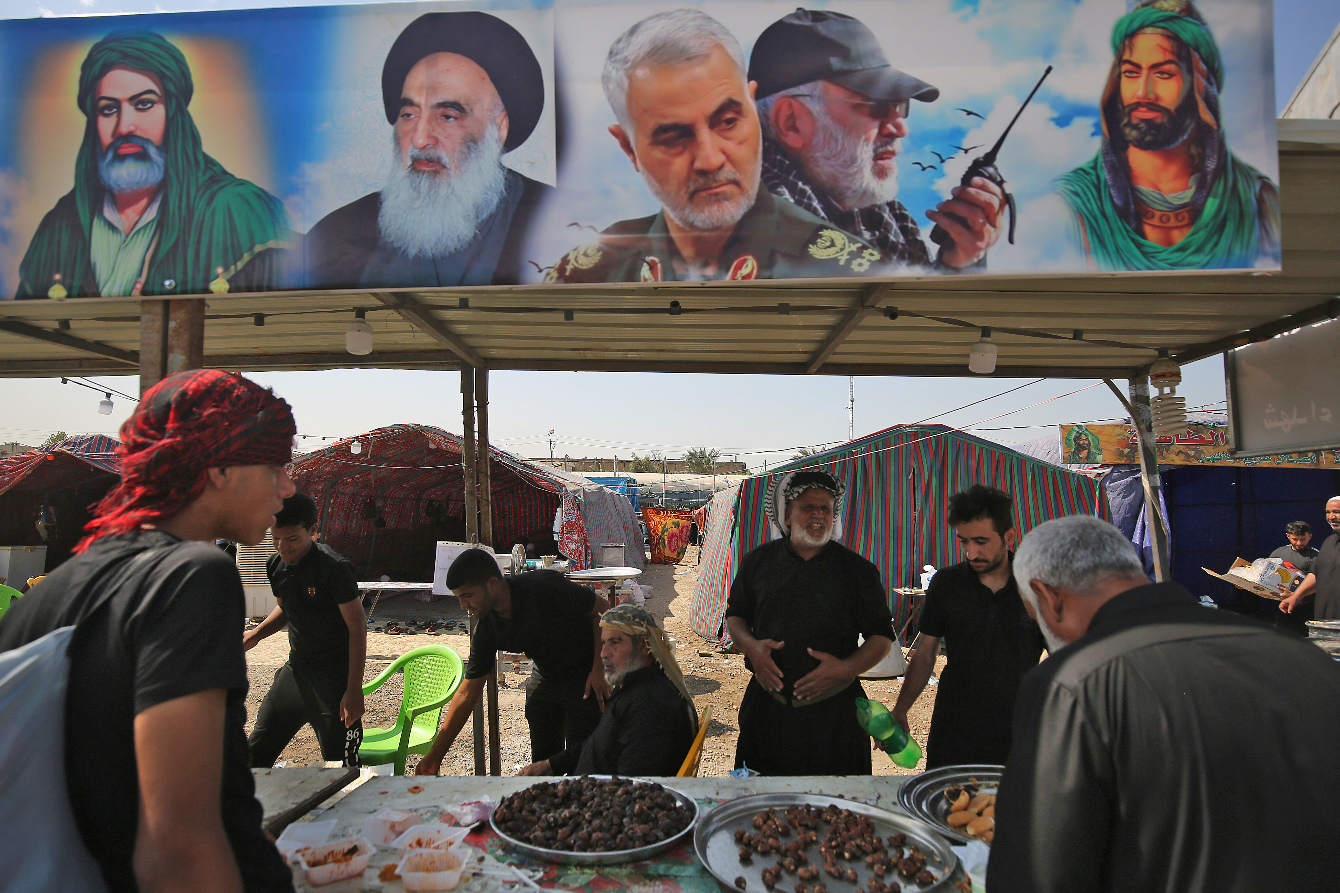 Iraqi Shia Muslim pilgrims stop at a tent adorned with portraits of Abu Mahdi al-Muhandis (2nd from right) and General Qassem Soleimani (center) at Baghdad's al-Dora area as they head to the holy city of Karbala to take part in Arbaeen, Oct. 5, 2020. (Photo: AFP/Mohammed Sawaf)